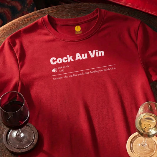 Red t-shirt with 'Cock Au Vin' text on a wooden bar table with wine glasses.