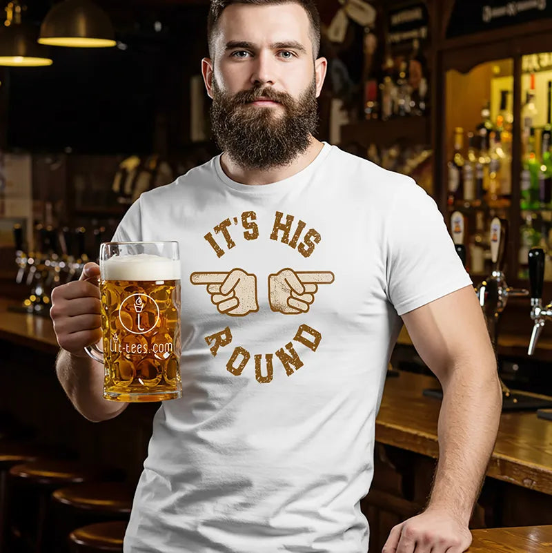 Man holding a beer mug in a bar wearing a t-shirt with a graphic design and text saying 'It's his round'
